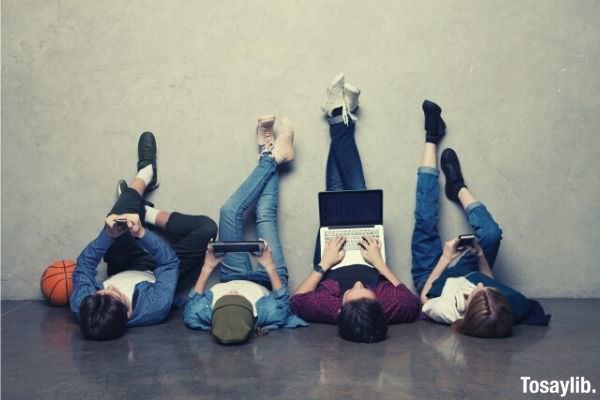 four people lying while raising their feet on the wall using gadgets