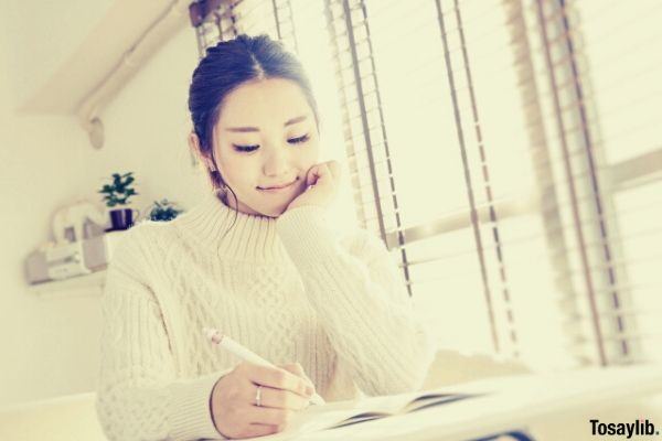 image of a woman wearing white sweater holding pen writing on a notebook