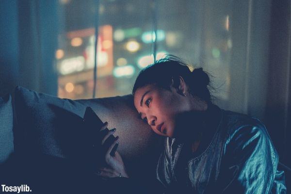woman using mobile phone leaning on the pillow night time