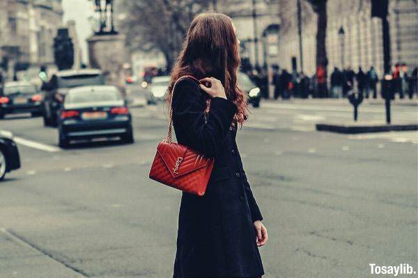 woman in black coat and red leather sling bag standing near sidewalk