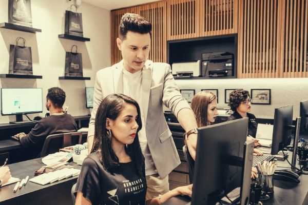 man-in-formal-suit-pointing-something-at-the-monitor-teaching-a-woman