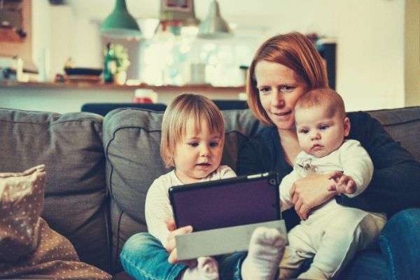 two babies and their mom sitting on the sofa while watching on the tablet