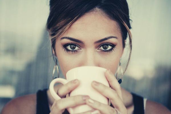 woman-drinking-coffee-on-a-white-coffee-mug-looking-at-the-camera