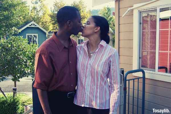 husband in red polo kissing wife in stripe blouse outside the house