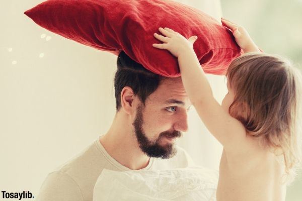 photo of a child putting red pillow on the head of his dad