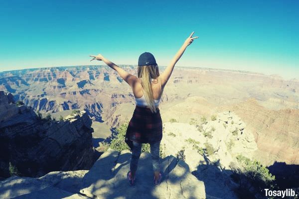 woman in tank top with cap raising her hand on top of concrete beautiful view