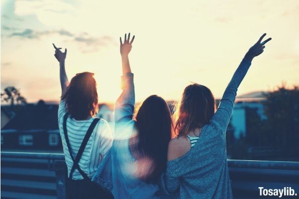 three friends wearing jacket and jumper raising their hands happy sunset