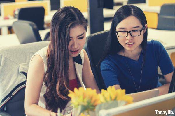 two girls looking at the laptop sleeveless and blue shirt with glasses