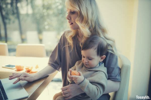 woman carrying her baby and working on a laptop