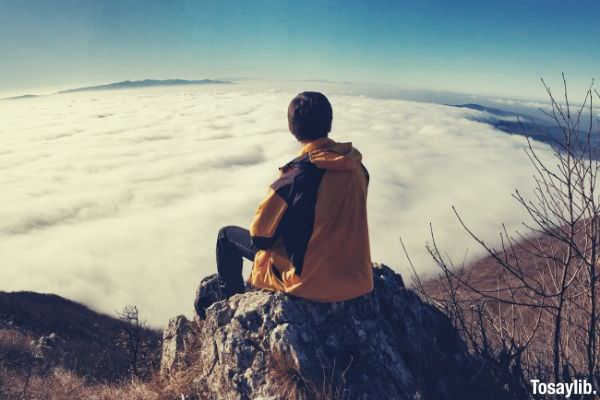 man sitting on the rock looking at the sea of clouds