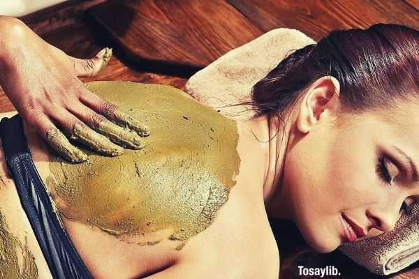 person massaging a red haired woman with mud