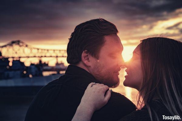 man black sweater woman kissing sunset bridge