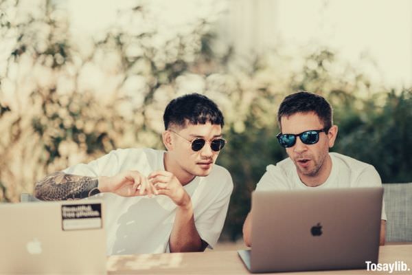 two men wearing white shirt sitting near the table using macbooks