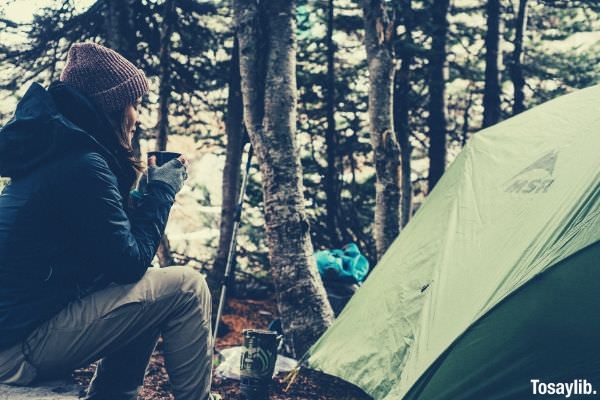 woman with bonnet sitting near tent with a cup of coffee