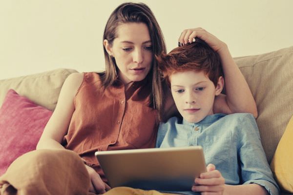 photo-of-woman-and-boy-watching-through-tablet-computer-while-sitting-at-the-sofa