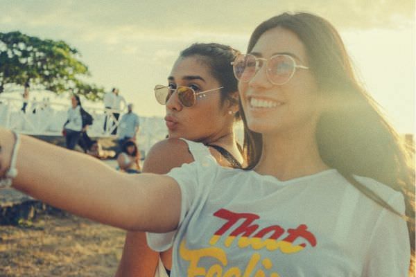 two women friends wearing sunglasses taking a selfie of theirselves and sunset