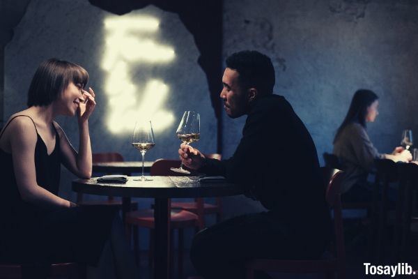 man in black long sleeve shirt sitting on a chair having wine with a lady