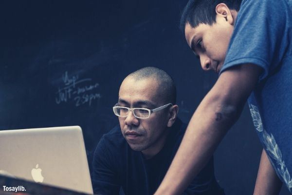 two men watching on macbook black background serious