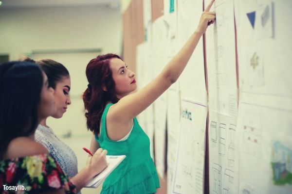 woman wearing green sleeveless pointingpaper board two women looking