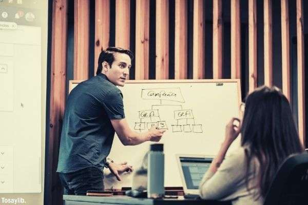 man wearing gray polo writing on the board while the girl is listening