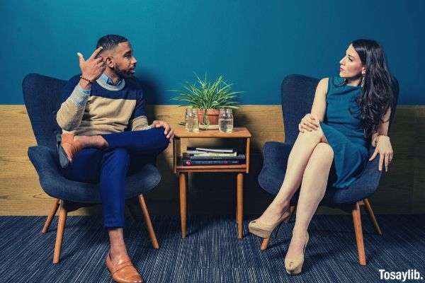 woman wearing teal dress sitting on chair talking to man in semi formal clothes