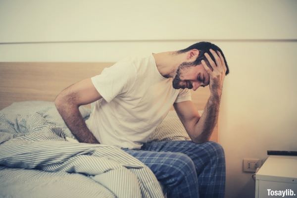 young man sitting on the bed touching his head headache