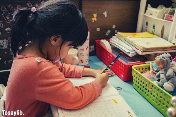 Girl in orange long sleeves writing on a work book on her study table