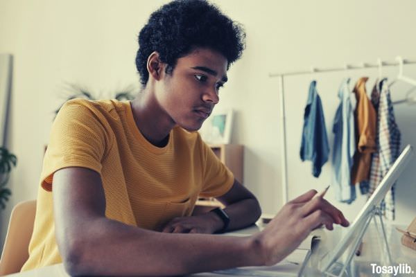 man in yellow crew neck t shirt while using tablet hanging clothes on the background