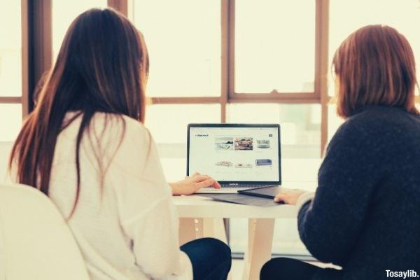 two women sitting in front of the laptop computer while talking