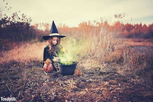 Girl in witch costume sitting on dried field