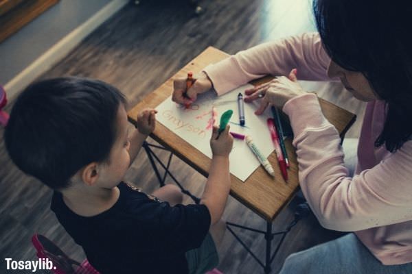 boy boy in black shirt writing with green pen mother in pink long sleeves writing using color