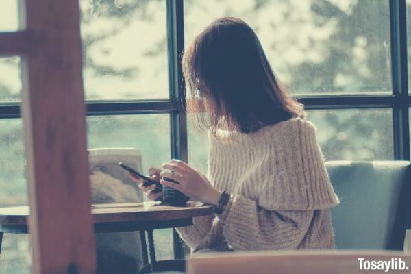 woman with eyeglasses sitting on chair and using smart phone on coffee table