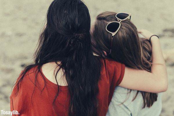 two women sitting on a tree trunk putting each arms on one another