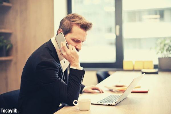 man wearing formal suit having a phone call in front of a laptop sitting