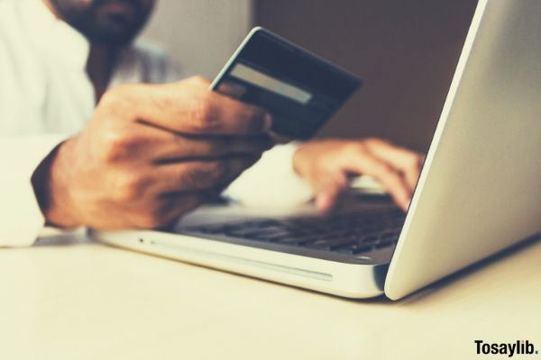 person looking at his credit card while typing on the laptop