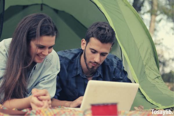 young couple browsing netbook at campsite outside the tent