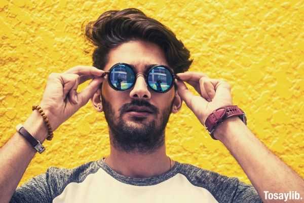 man in white and gray shirt wearing sunglasses against yellow wall