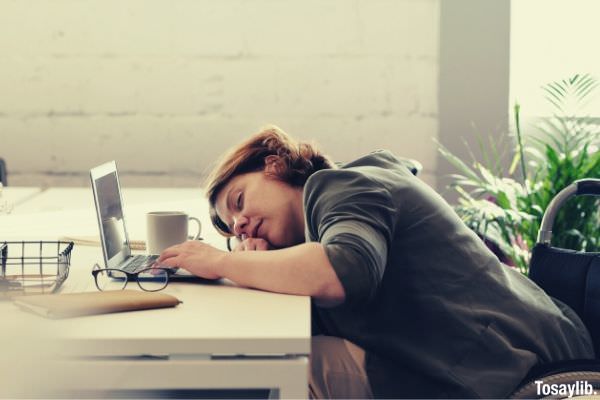 woman tired sleepy eyes leaning on the table while using laptop