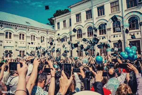 graduates throwing their hats with blue ribbon many people smartphones taking photo