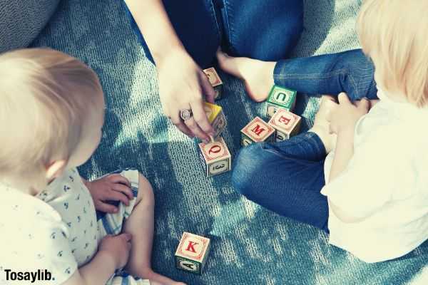 two blonde haired toddlers playing letter cubes with their mom