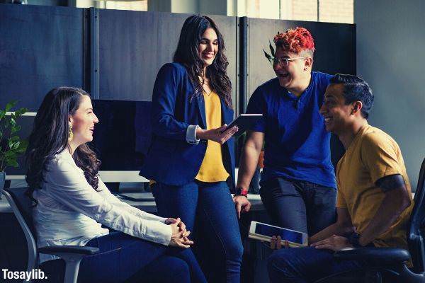 group of people smiling in the office two people sitting and another standing holding tablet