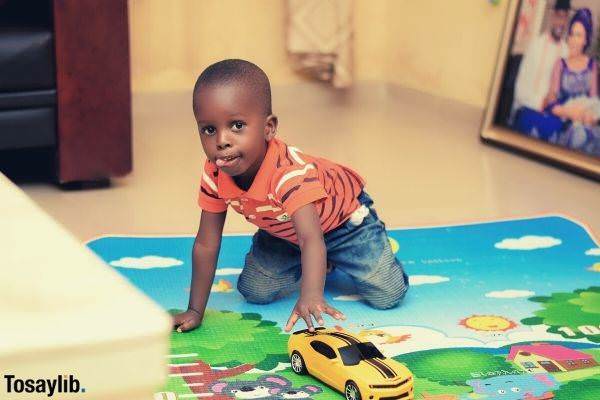 cute boy wearing orange stripes playing a chevy camaro toy car on the floor