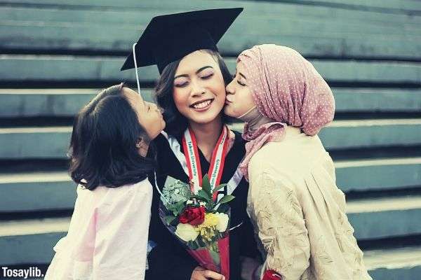 two girls kissing woman in graduation gown holding flower