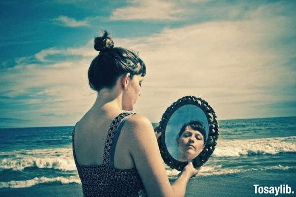 woman in sleeveless on the beach looking at the mirror