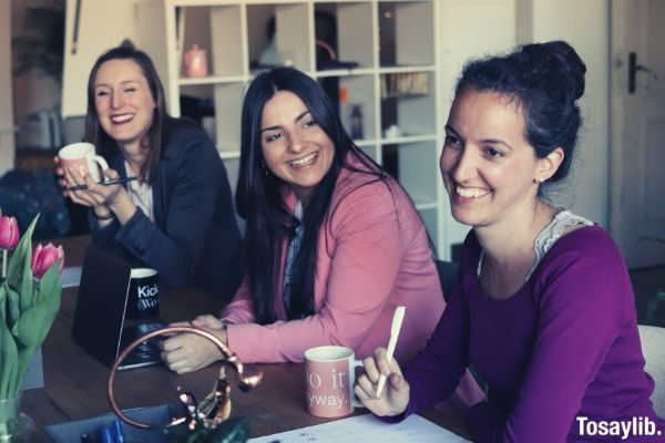 three women sitting by the table smiling having cup of coffee
