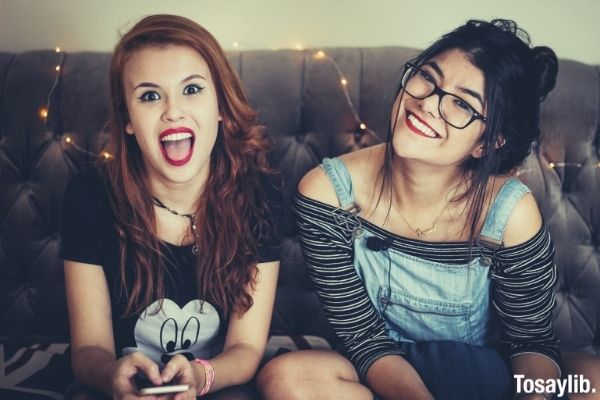 two cute women smiling one wearing black shirt and one on jumper sitting on the sofa