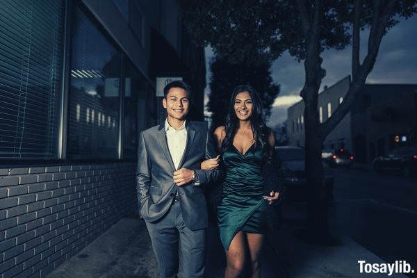 man in gray suit standing beside a woman in green dress going to homecoming party