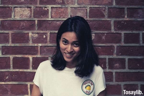 beautiful woman smiling wearing white shirt with taco me out logo printed brick wall