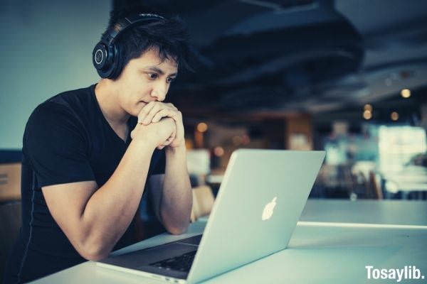 man wearing black shirt and black headphones sitting in front of macbook while watching