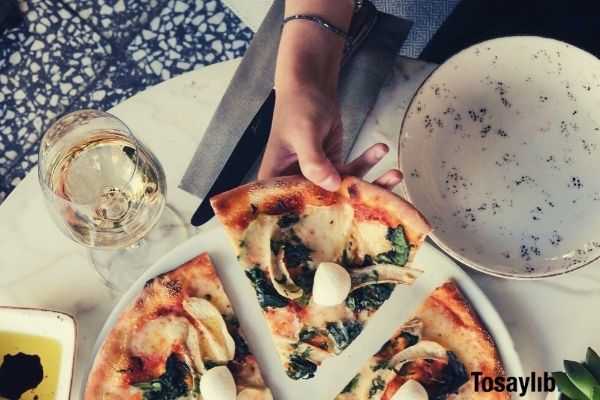 woman wearing black blouse and bracelet getting a slice of pizza on the plate